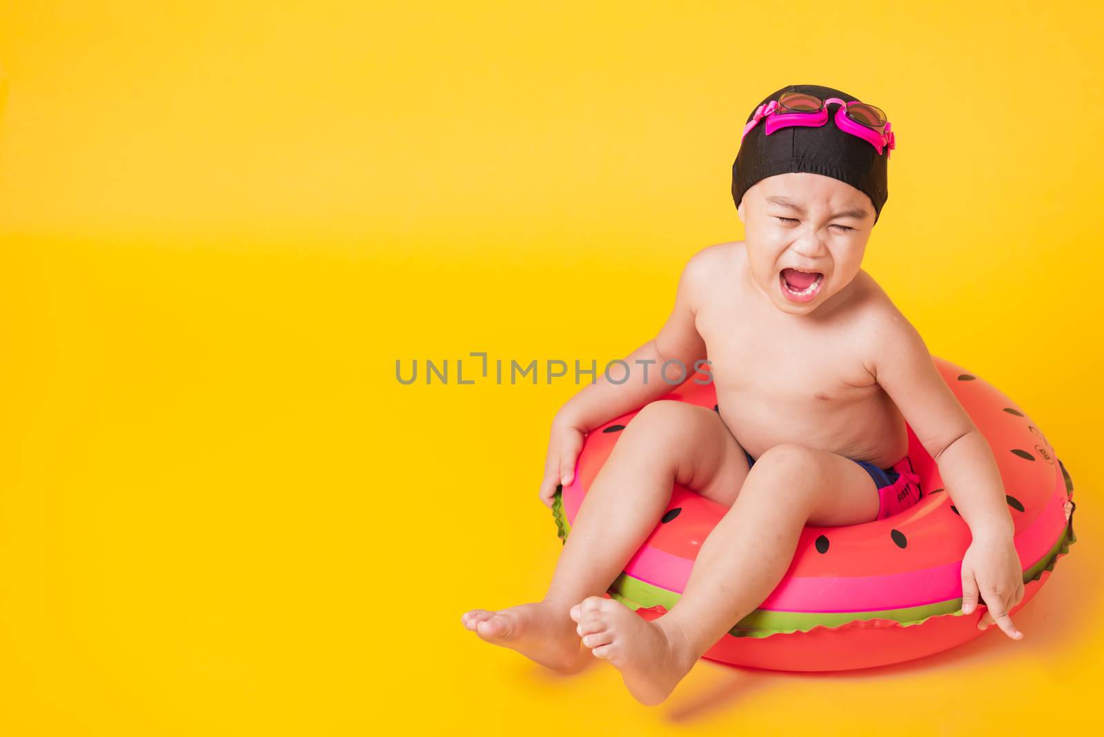 Summer vacation concept, Portrait Asian happy cute little child boy wear goggles, swimsuit hold beach watermelon inflatable ring, Kid have fun sit in inflatable, studio shot isolated yellow background