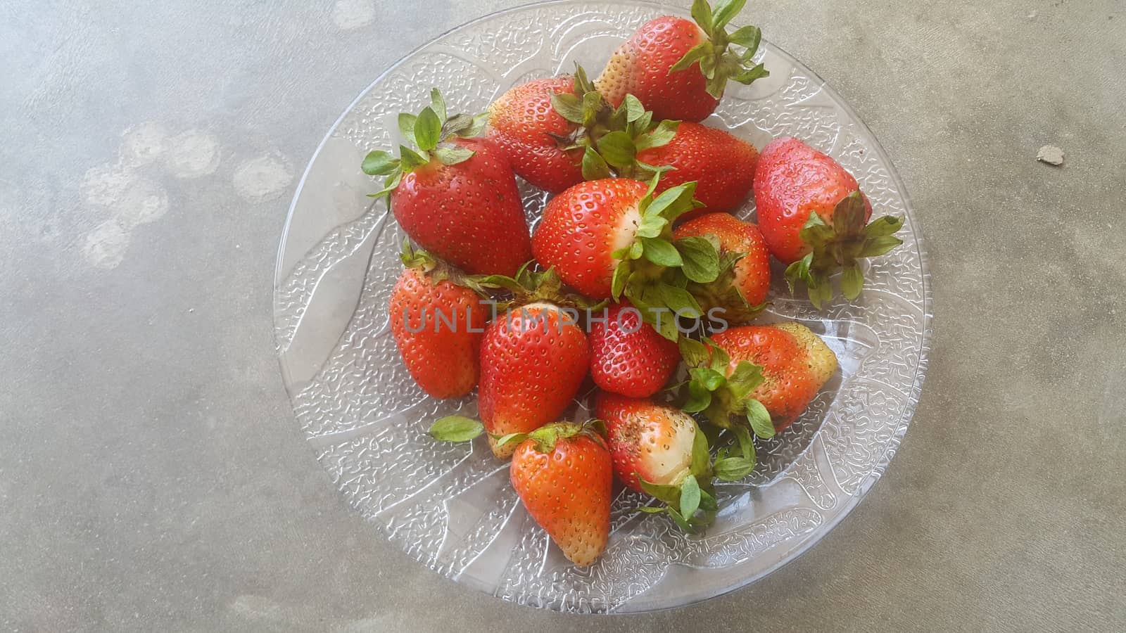 Top view with selective focus of sweet fresh strawberries with green leaves in plate on grey floor background.