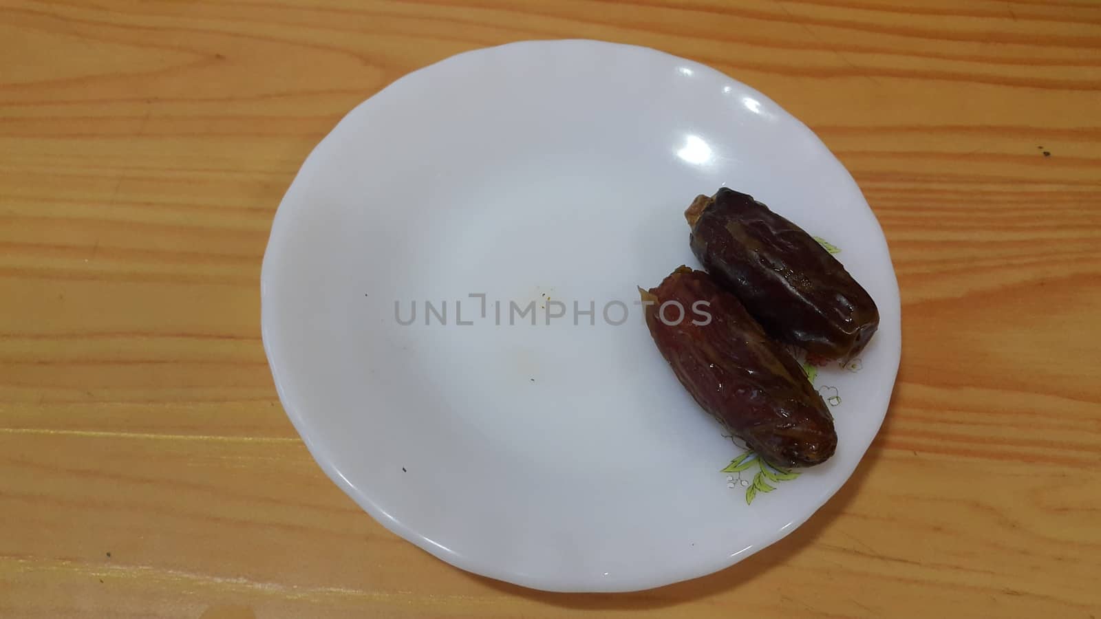 Close up view of fresh dried date palm served in ceramic small white plate over a wooden floor