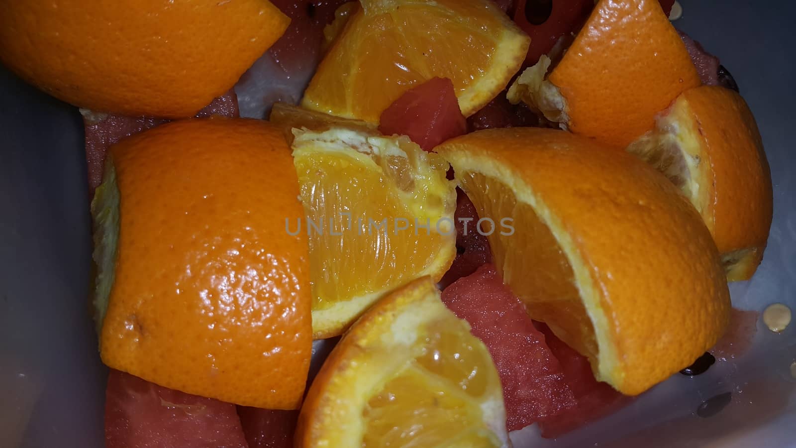 Closeup view of mixed fruits slices of oranges and red water melon served in a ceramic white plate. Water melon is sweet while oranges are citrus in taste