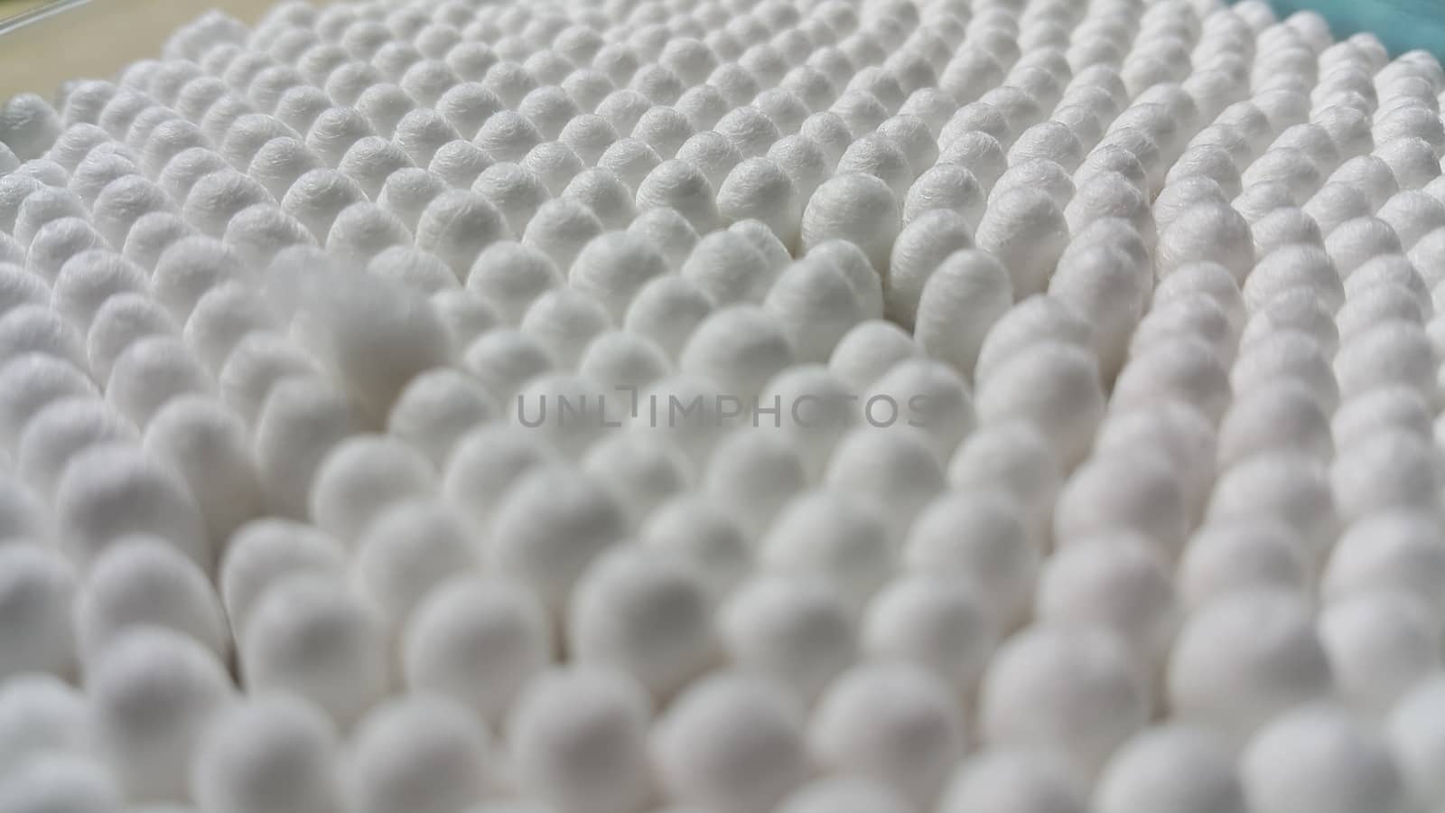 Closeup view of several cotton buds heads arranged in rows and columns. The cotton buds consist of one small wad of cotton wrapped around one or both ends of a short rod made of wood or plastic.