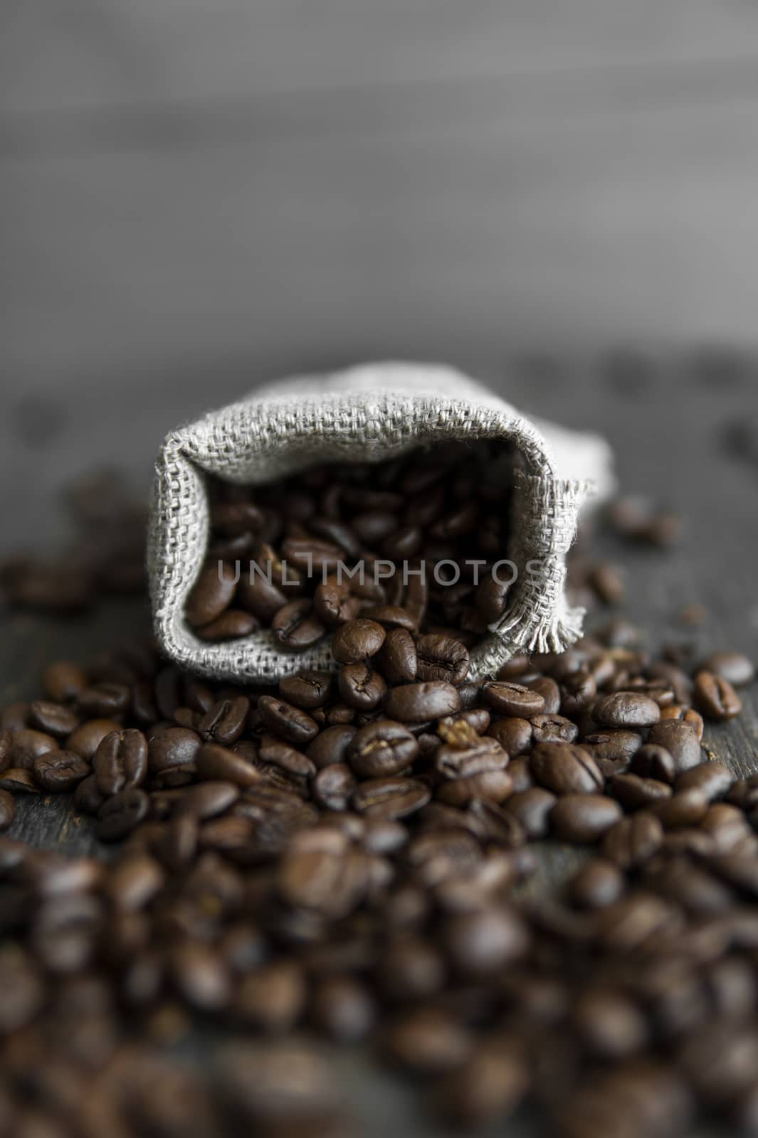 Coffee beans scattered from a linen bag on a wooden table. Fresh roasted arabica coffee beans