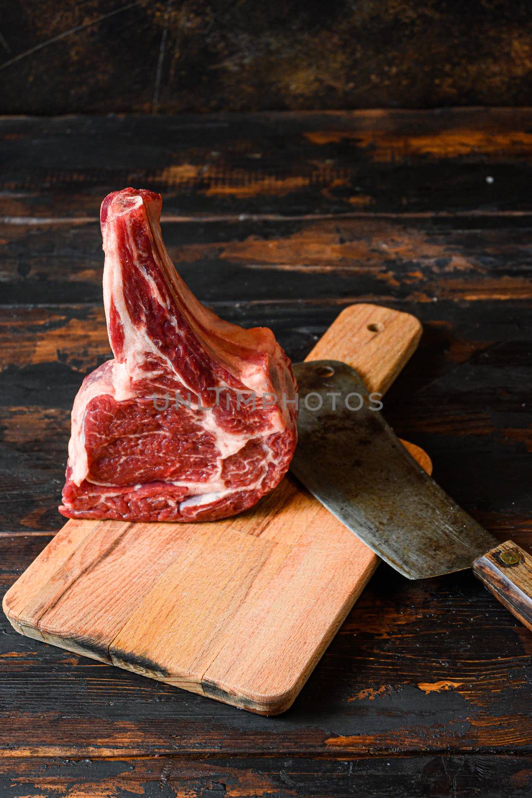 Raw Dallas black angus or spencer marbled steak in butchery side view over choping board with old american cleaver rustic old cutting board with dark planks by Ilianesolenyi