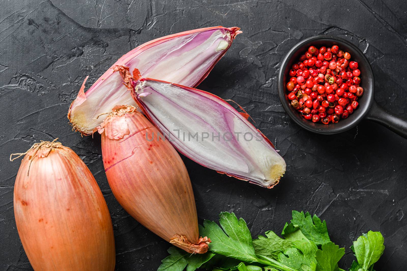 Organic shallot, bio eschalot or farm scallion raw ripe onions with greens and rose peppercorns sliced and halved black concrete textured background top view.