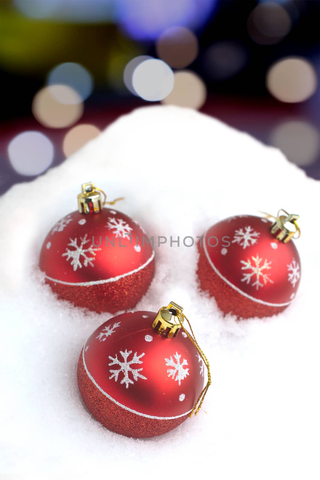 Red Christmas balls with painted snowflakes lying in clean white snowdrift against color circles on dark background vertical view closeup