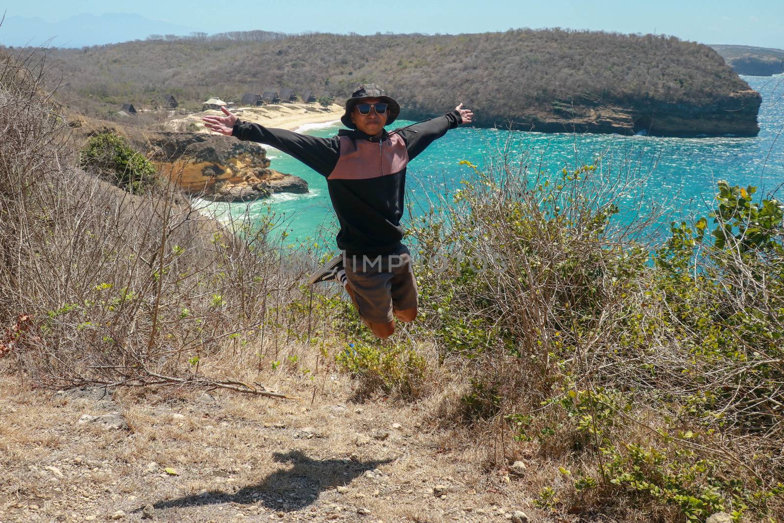 Man jumping cliff against sea with blue sky. A young man is jumping on the beach, Having fun, Summer vacation holiday lifestyle. Happy teenager jumping freedom. Asian guy in shorts and a T-shirt.
