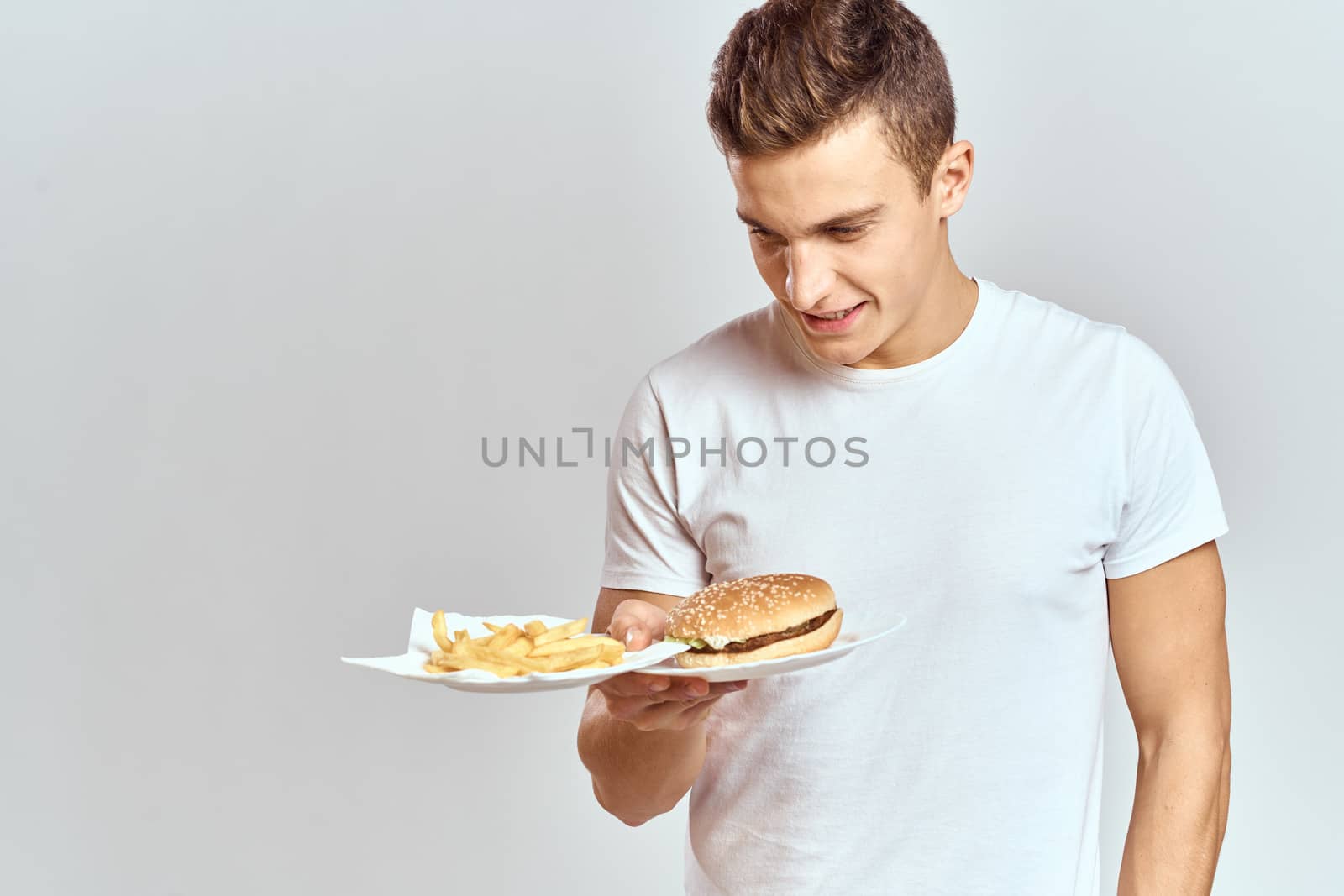 a man with fries and a hamburger on a light background in white t-shirt close-up cropped view Copy Space Model by SHOTPRIME