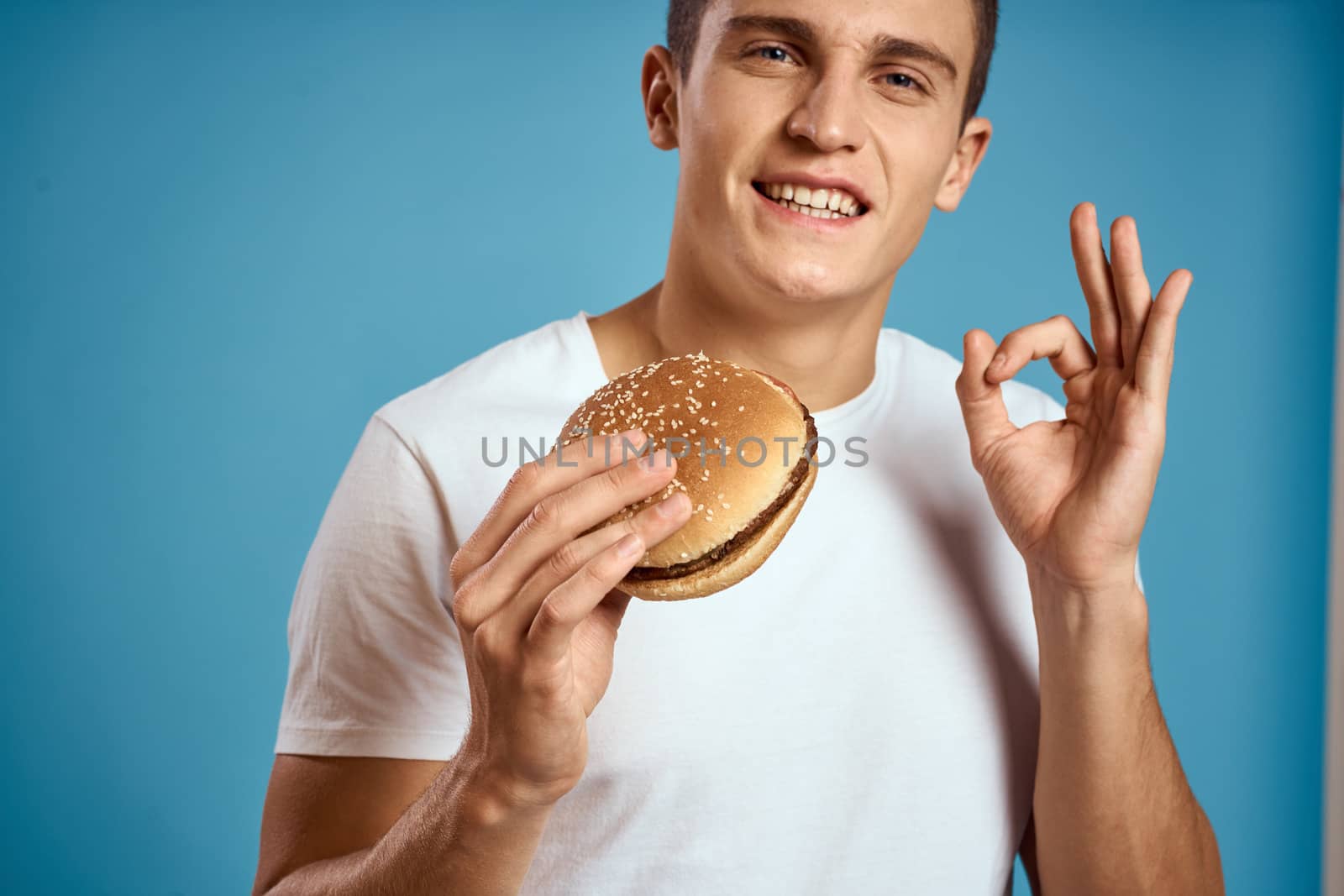 man with hamburger and white t-shirt blue background emotions gesturing with hands Copy Space by SHOTPRIME