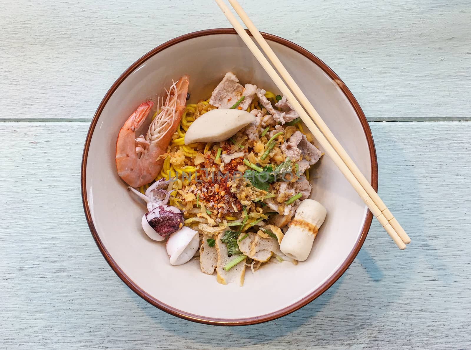 Noodle in a bowl, with shrimp, and squid, and chili, and vegetable, on wooden table, blurred background
