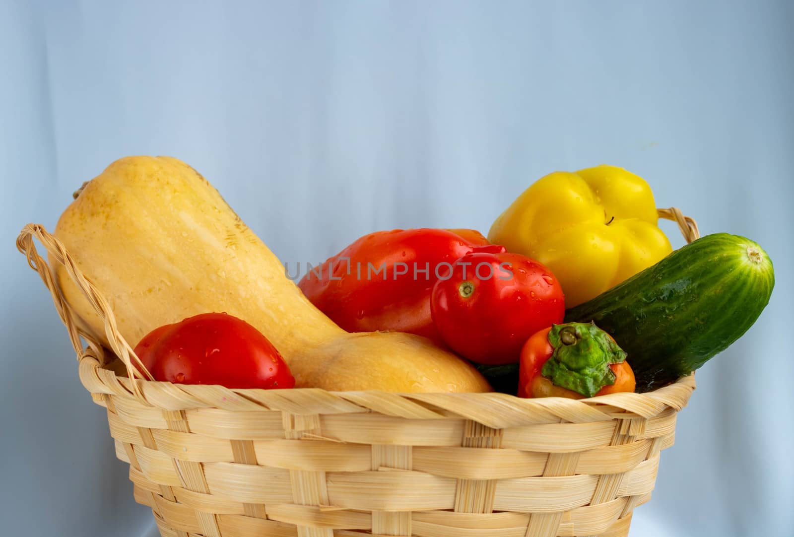 Wicker basket with different vegetables. Pumpkin, pepper, cucumber, tomatoes.Isolated on a blue background.The concept of crop