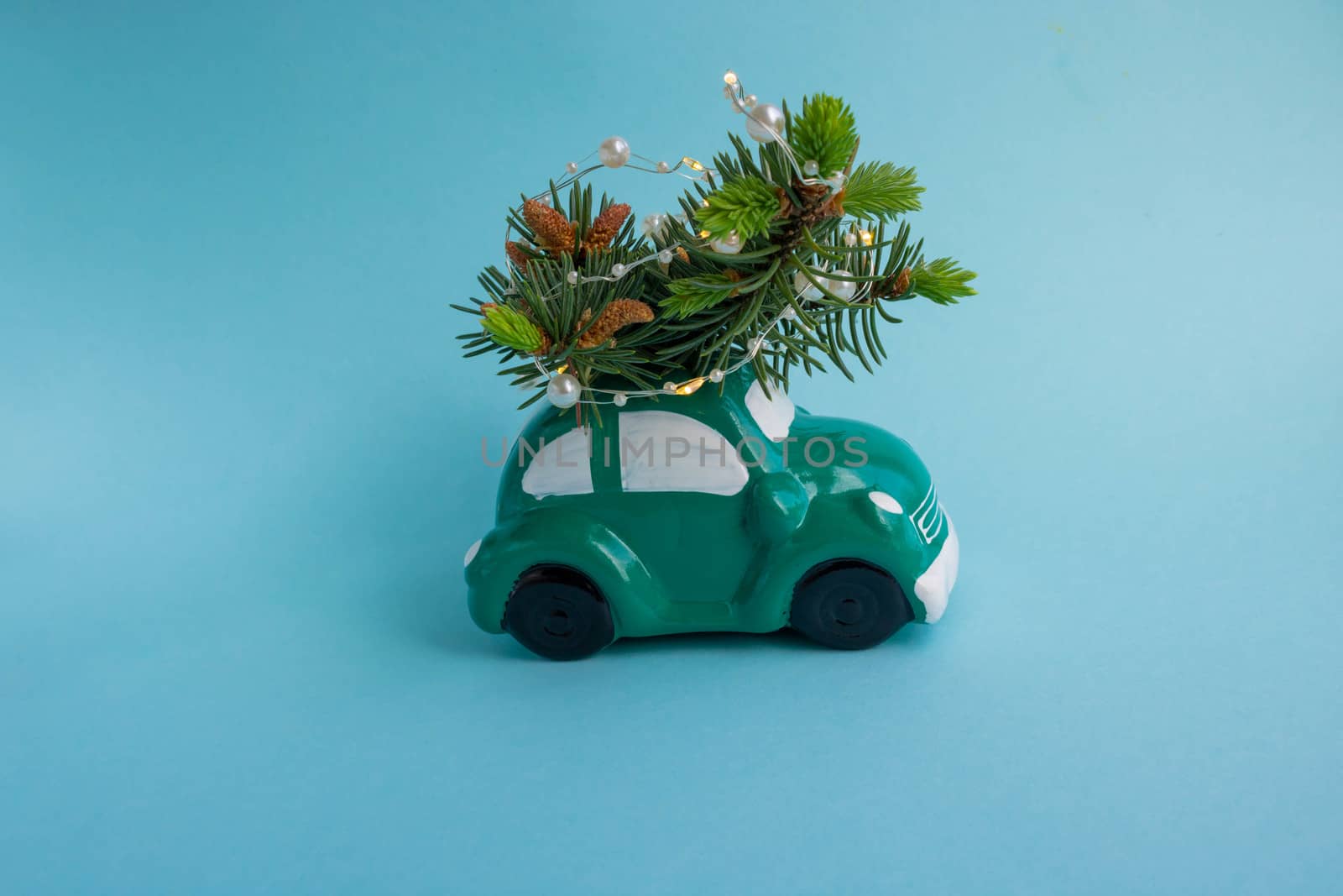 Green toy car-piggy Bank, carrying a Christmas tree on the roof with a garland on a blue background