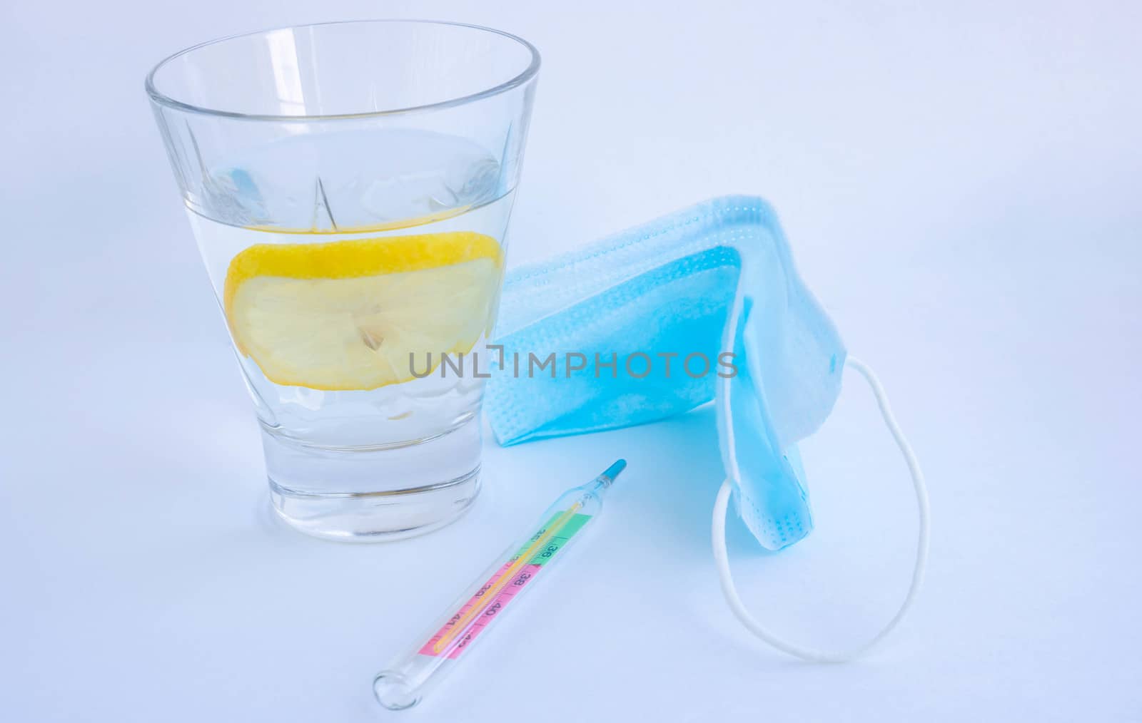 A glass of water with lemon, a mask and a thermometer on a white background. Glass mercury thermometer with high temperature by lapushka62