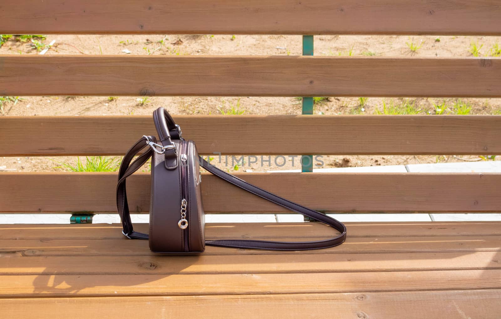 A woman's brown purse is lying on a light brown bench . Space for your text
