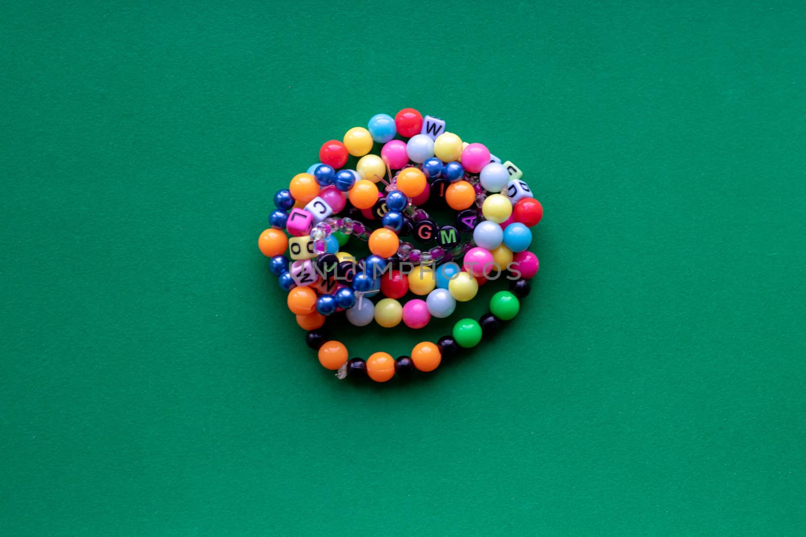 Eight multi-colored bracelets arranged in a flower shape on a green background. Bracelet with beads.