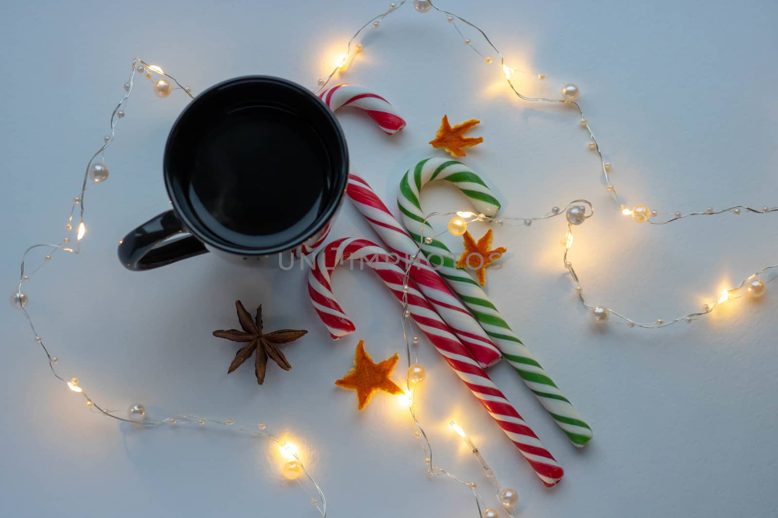 Christmas and winter concept. Black cup of hot coffee, candy cane and garland of white background.Top view. Holiday breakfast. by lapushka62