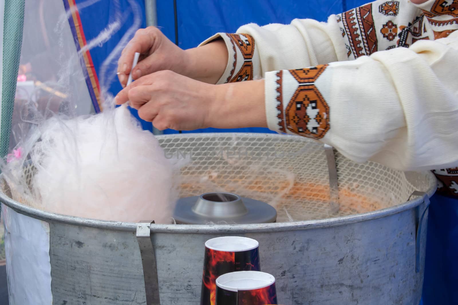 A person in latex gloves making pink cotton candy on a stick