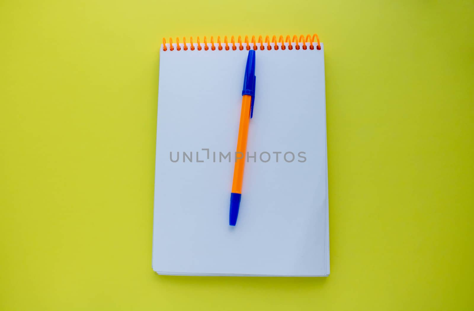 Notepad with an orange spiral and an orange pen, on a yellow background. top view copy space