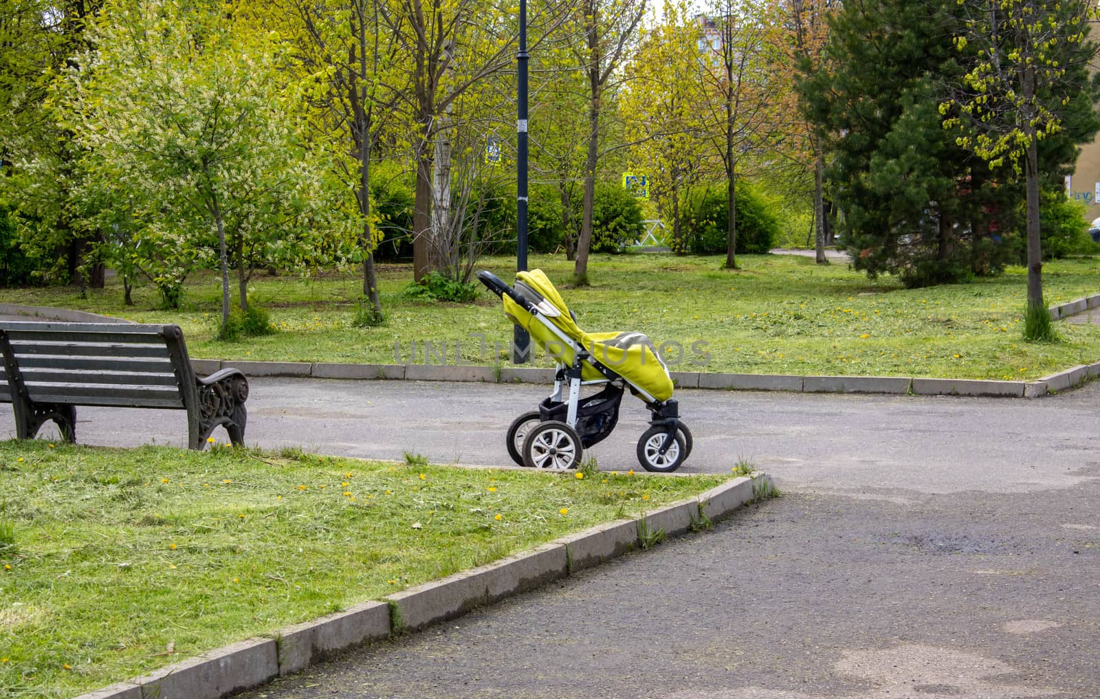 A green baby stroller stands in the middle of the Park. Travel with a child, transport a child, concepts of a child's walk.