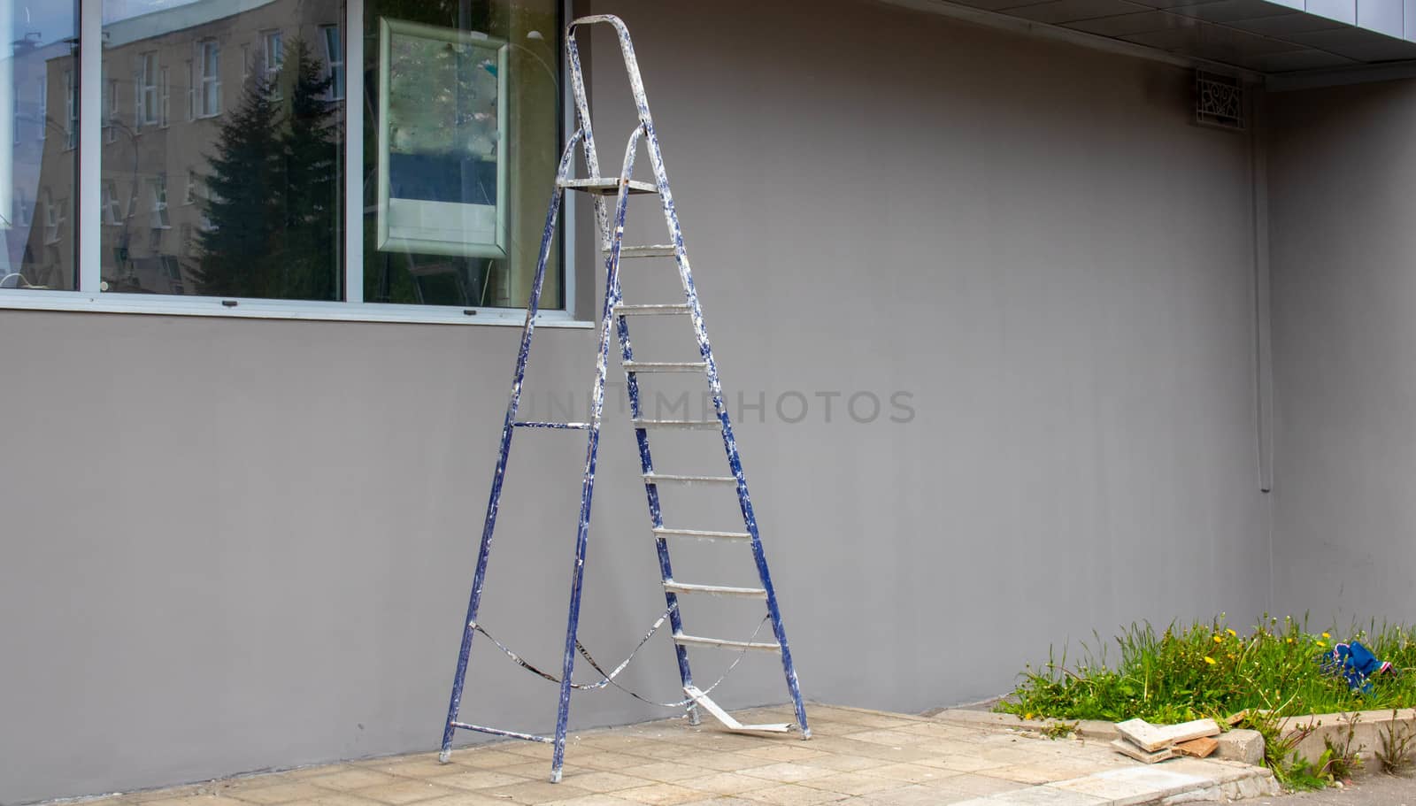 A construction ladder for work stands next to the facade of a gray building. Outdoor. Step ladder-platform