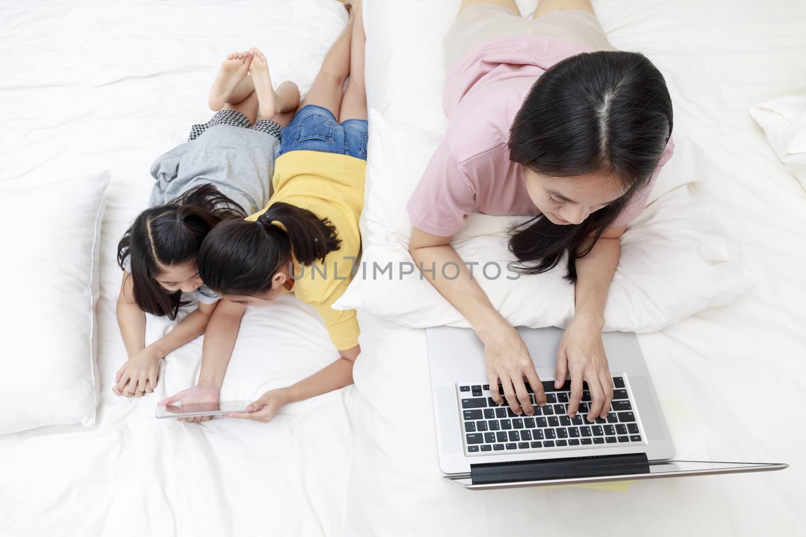 Asian mother and daugthers looking laptop and tablet on bed in bedroom. Business women woking with laptop at home with her daugthers smiling enjoy with tablet on bed. Work at home concept.