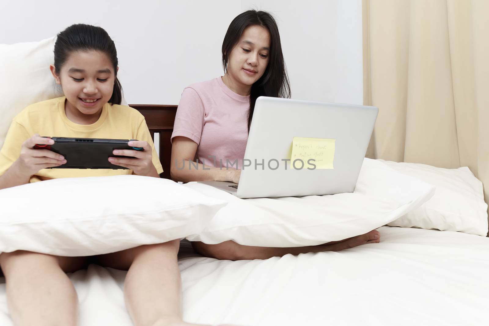 Asian mother and daugther looking laptop and tablet on bed in bedroom. Business women woking with laptop at home with her daugther smiling enjoy with tablet on bed. Work at home concept.