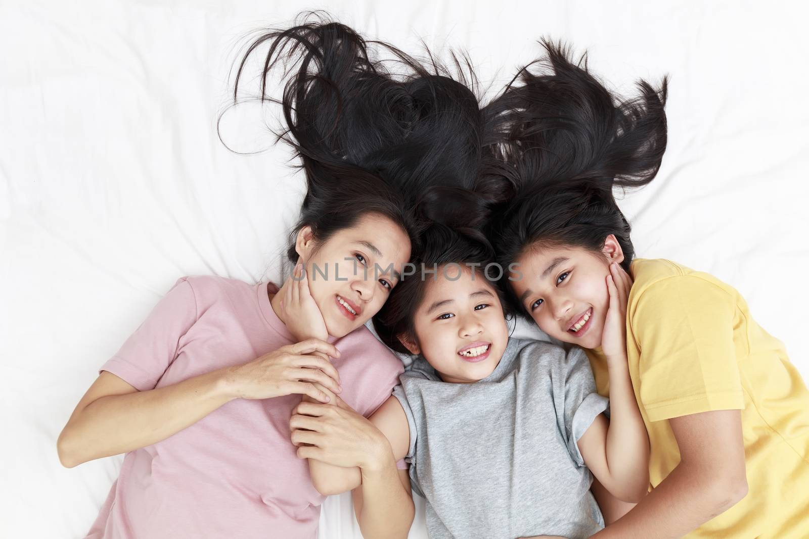 Top view Happy Asian family laying happy and smile on bed in bedroom. Mother and daughters enjoy smiling on bed