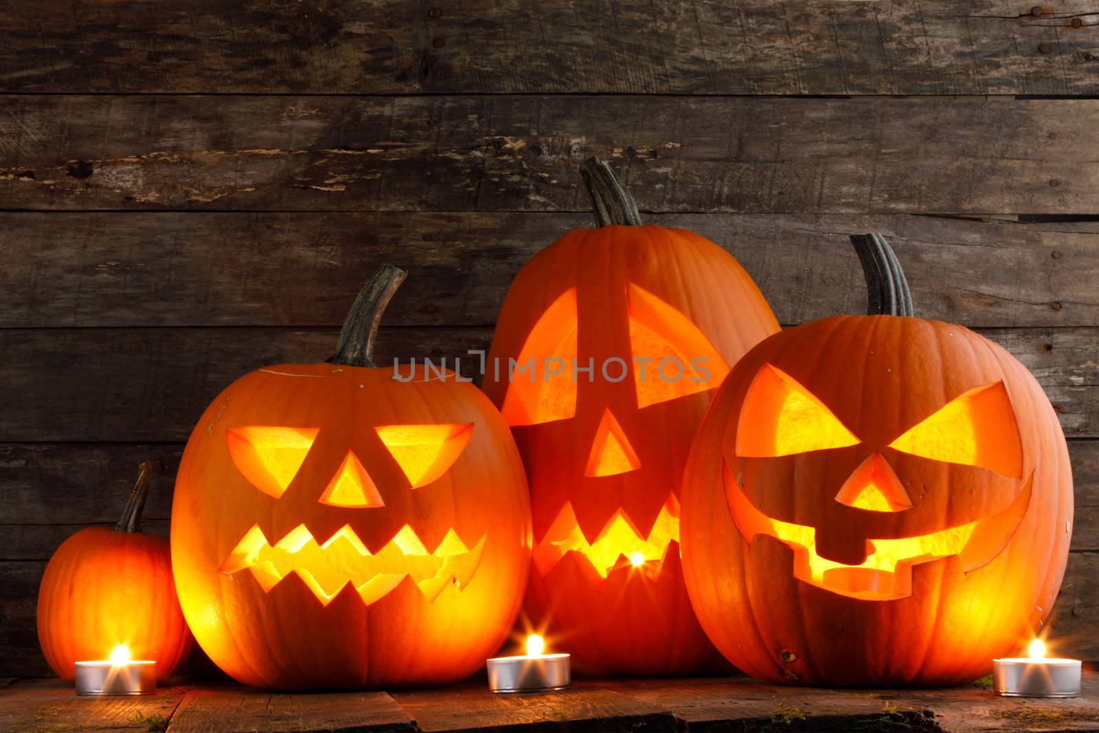 Halloween pumpkin head lanterns and burning candles on wooden background