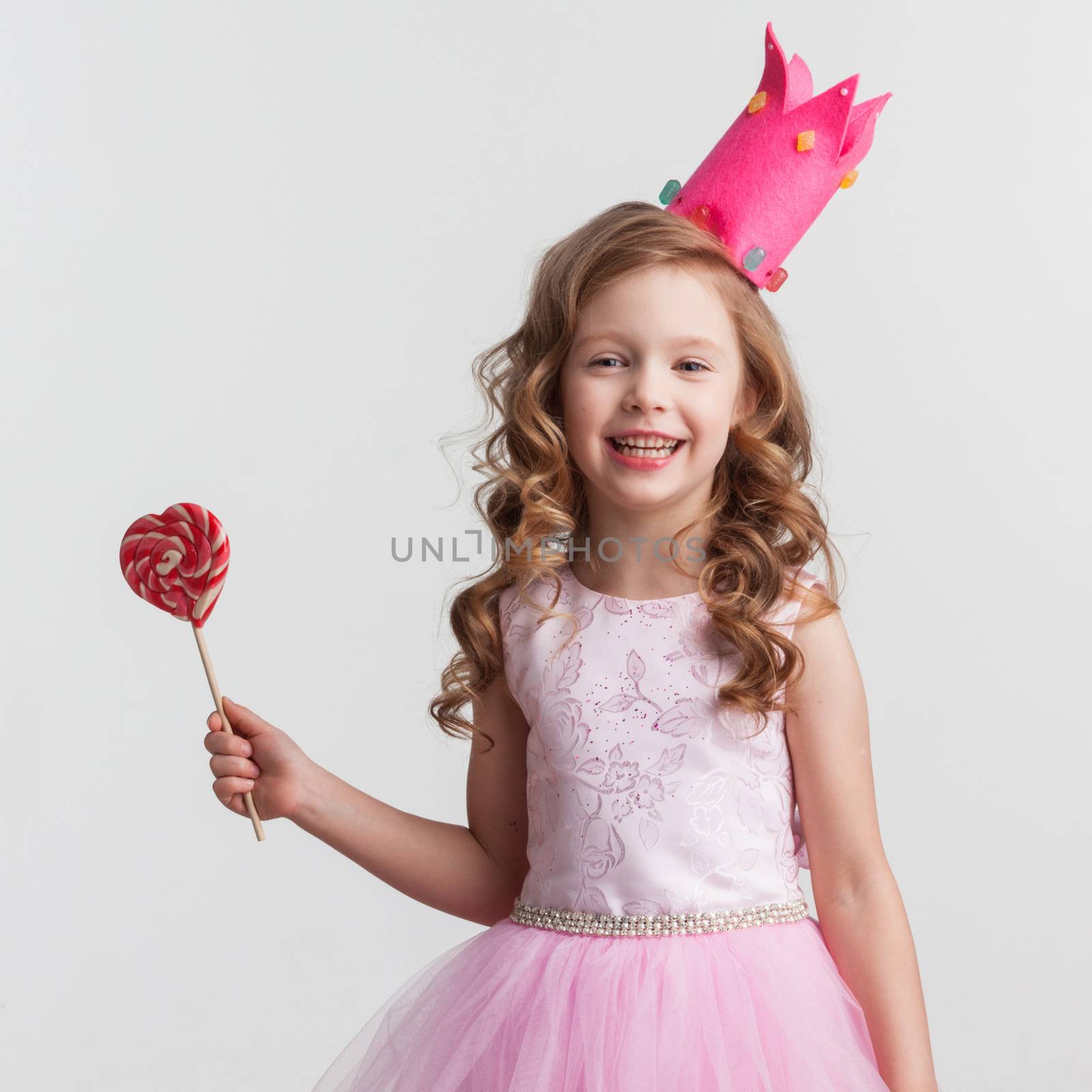 Beautiful little candy princess girl in crown with big pink heart lollipop
