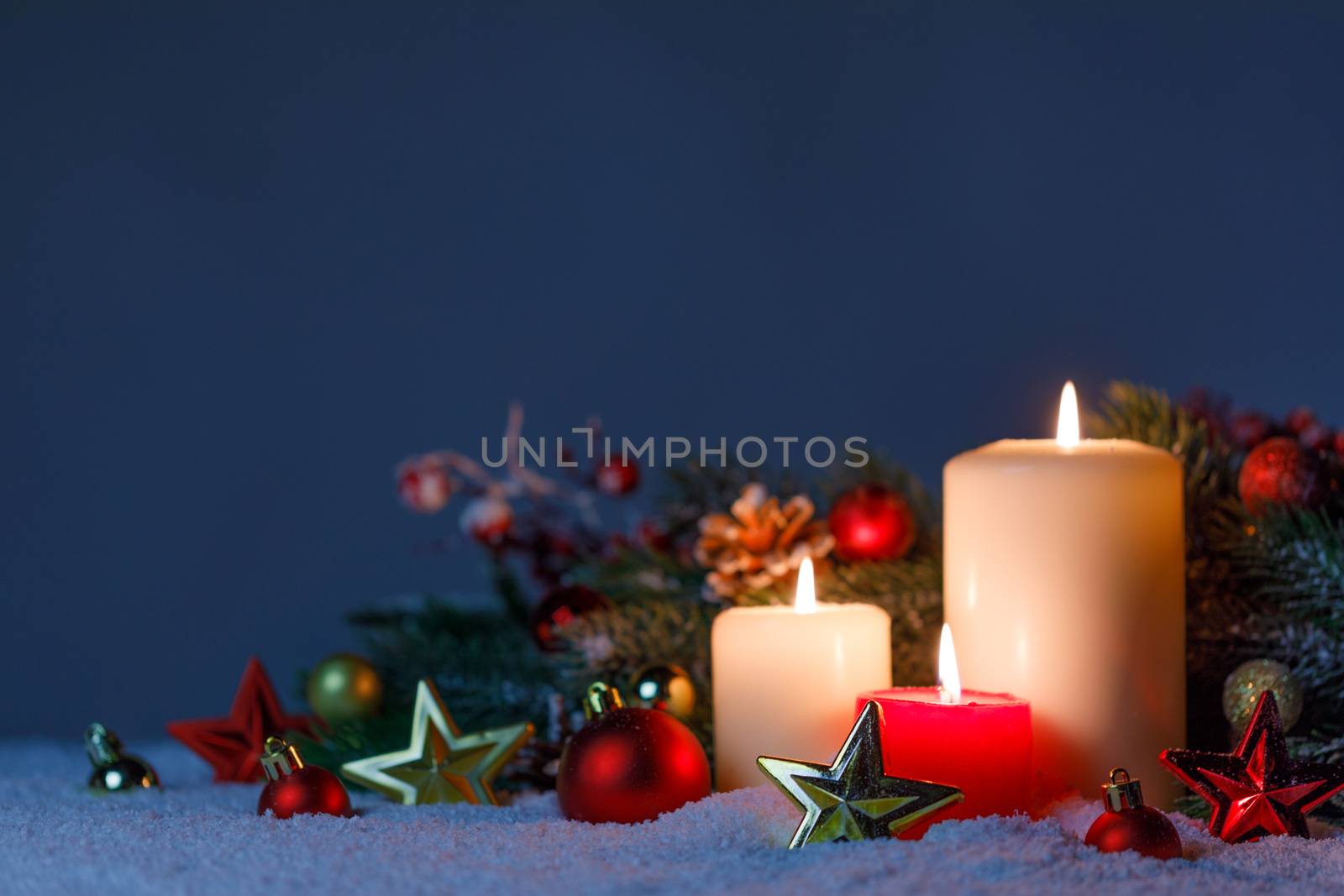 Burning christmas candles with red and golden decorative stars , baubles , pine cones and green branches on snow