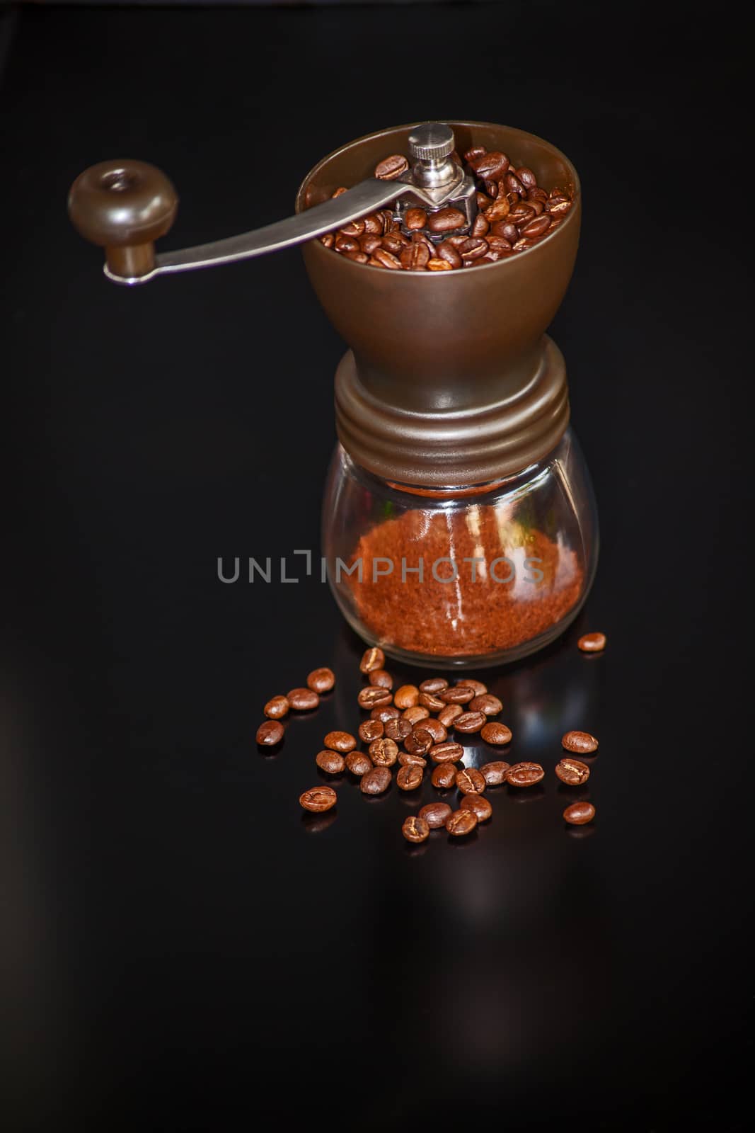 Hand operated coffee grinder with roasted beans on a black background.