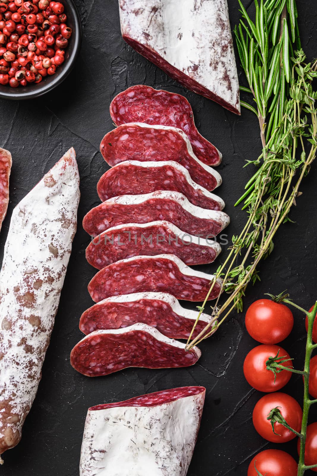 Set of various spanish dry cured salami sausages slices and whole cuts on black textured background.