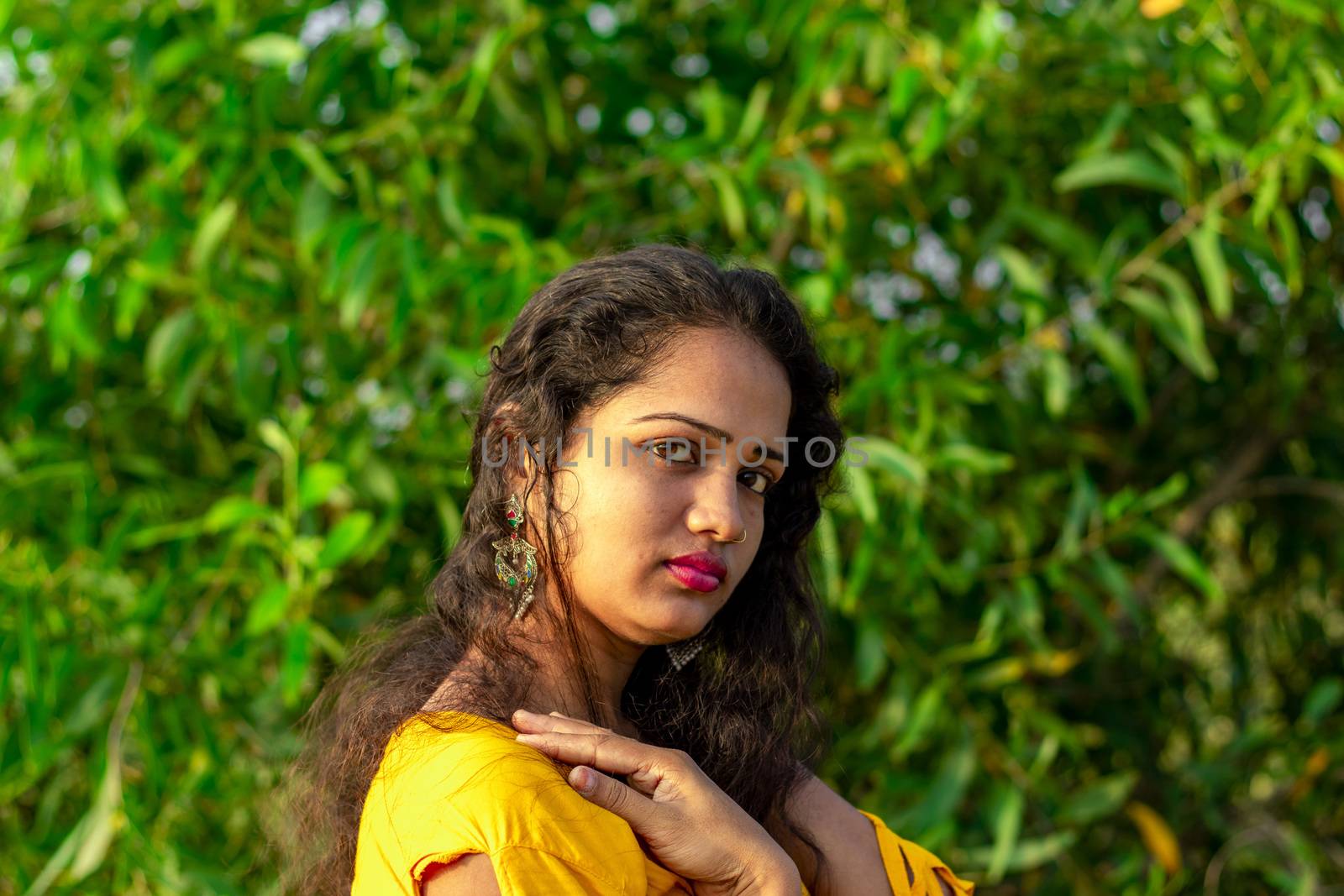 Photo of a beautiful woman face with natural light outside and green blurred background of tree leaves