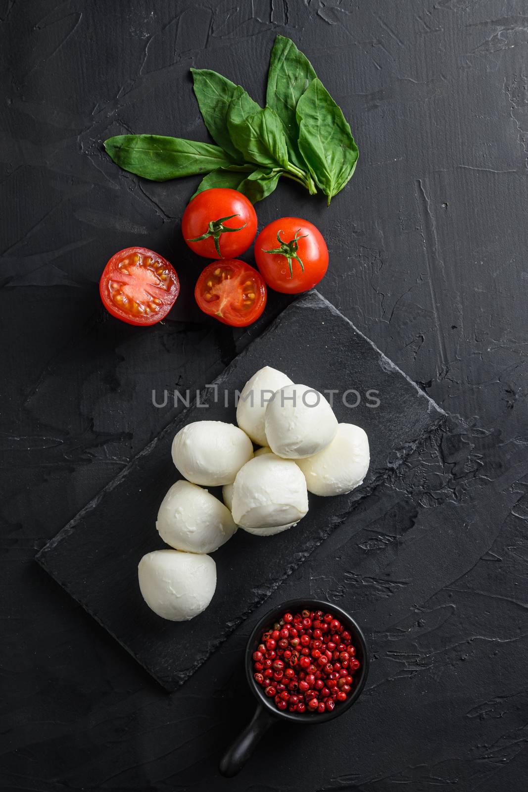 Fresh cherry tomatoes, basil leaf, mozzarella cheese on black slate stone chalkboard Healthy Italian traditional caprese salad ingredients. Organic Mediterranean food concept, flat lay space for text vertical by Ilianesolenyi