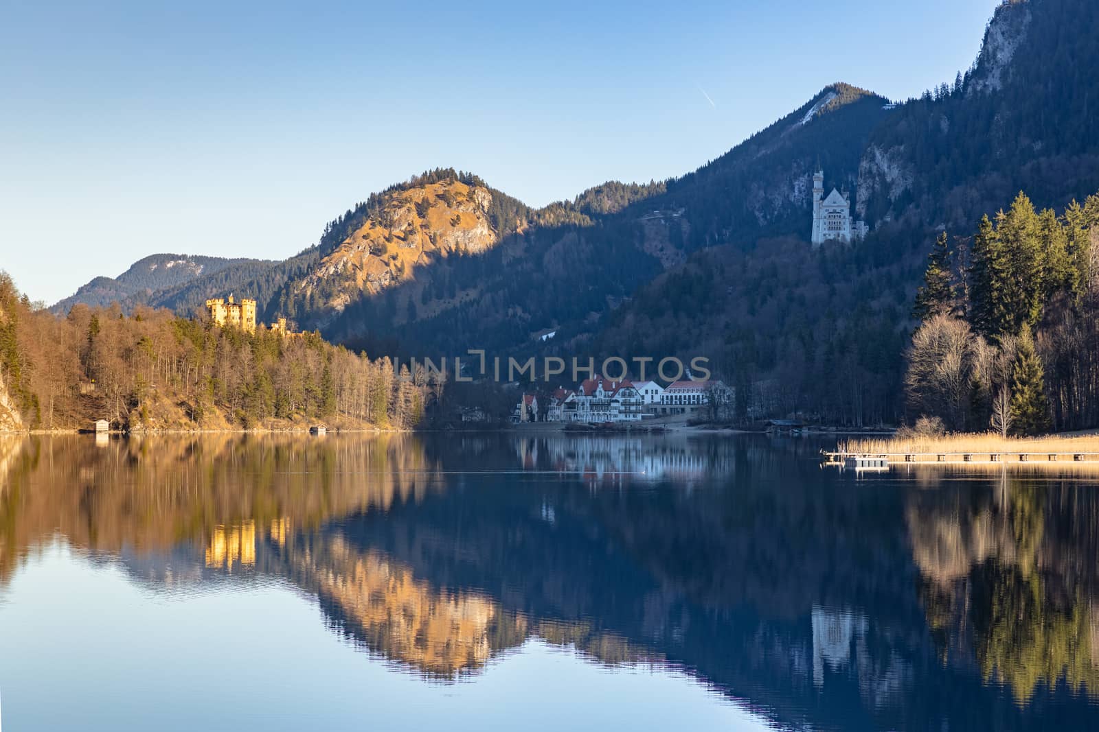 Stunning view of the Alpsee lake in winter on a sunny day with the Neuschwanstein Castle, Hohenschwangau Castle and Bavaria Alps in background, with beautiful reflections in water, Schwangau, Bavaria, Germany