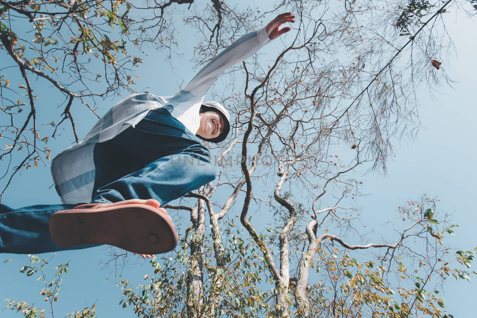 Low angle view of woman midair by jumping, crossing step over the camera shot below in forest with tree and sky overhead in concept travel, active lifestyle, overcome obstacles in life or future