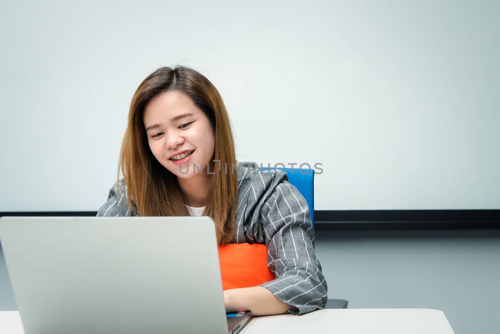 Asian woman is student, businesswoman working by computer notebook, laptop in office meeting room with whiteboard in background with happy and relax emotion in concept working woman, success in life