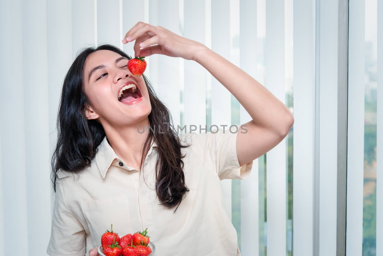 Asian pretty woman holding and eating fresh strawberry is red berry fruit color and sweet juicy with enjoy and happy emotion in concept food, healthy eating in life