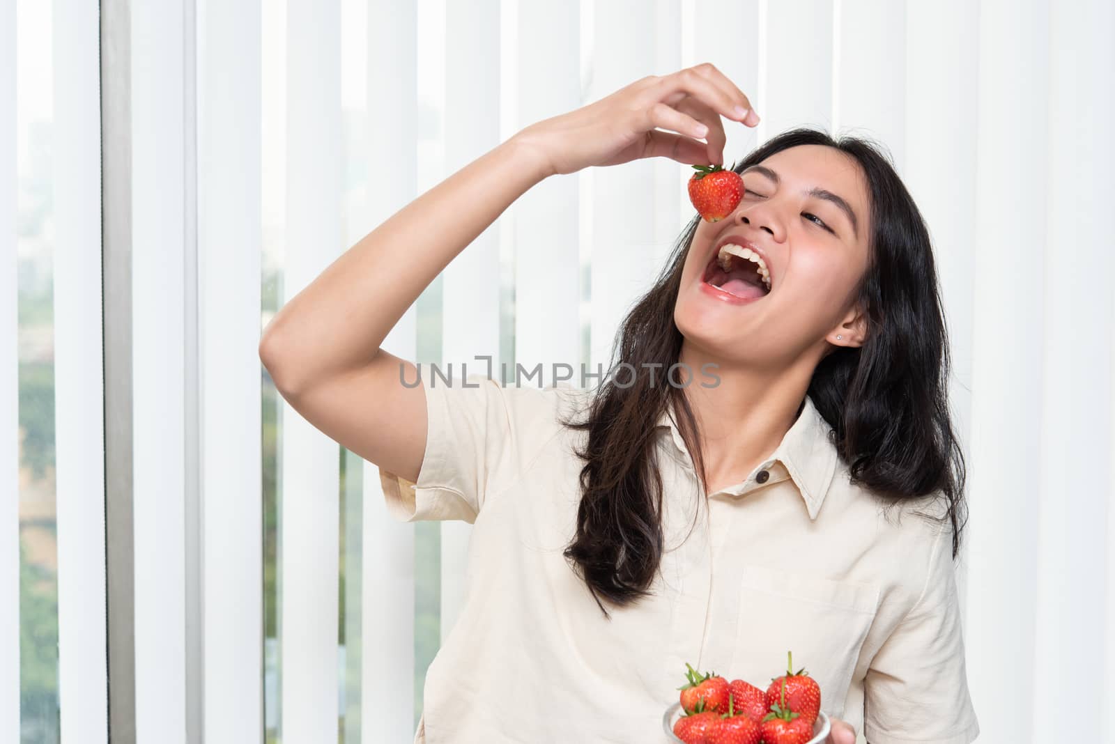 Asian pretty woman holding and eating fresh strawberry is red berry fruit color and sweet juicy with enjoy and happy emotion in concept food, healthy eating in life