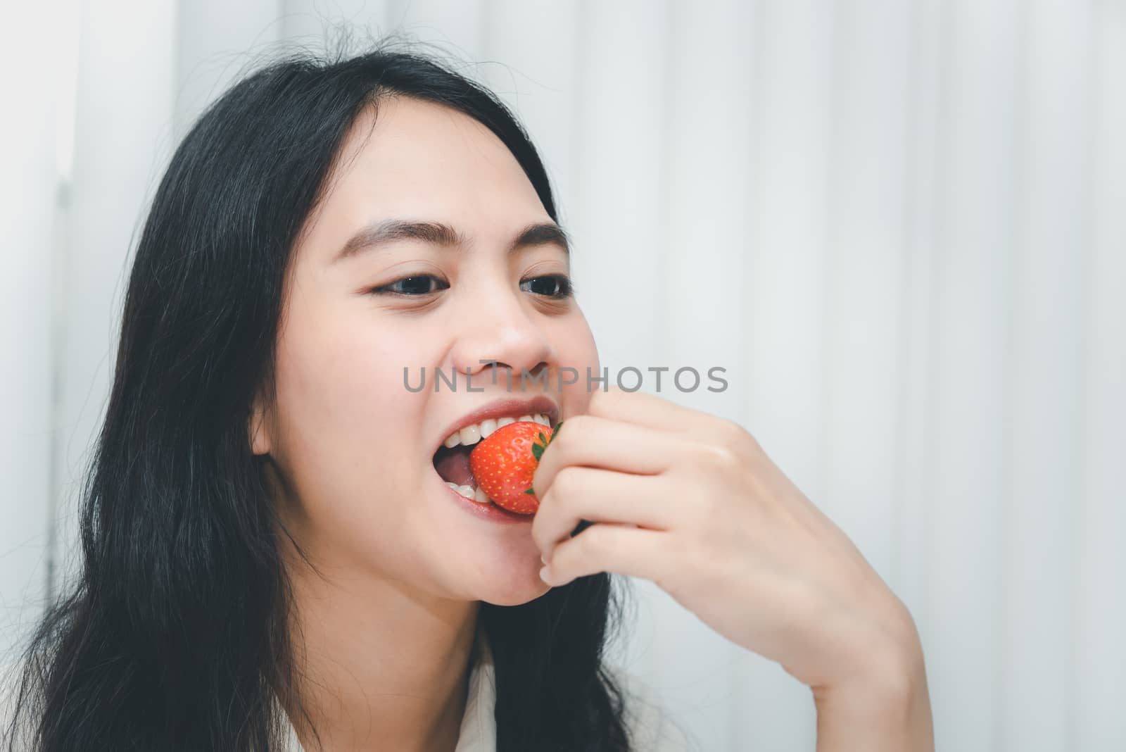 Asian pretty woman holding and eating fresh strawberry is red berry fruit color and sweet juicy with enjoy and happy emotion in concept food, healthy eating in life