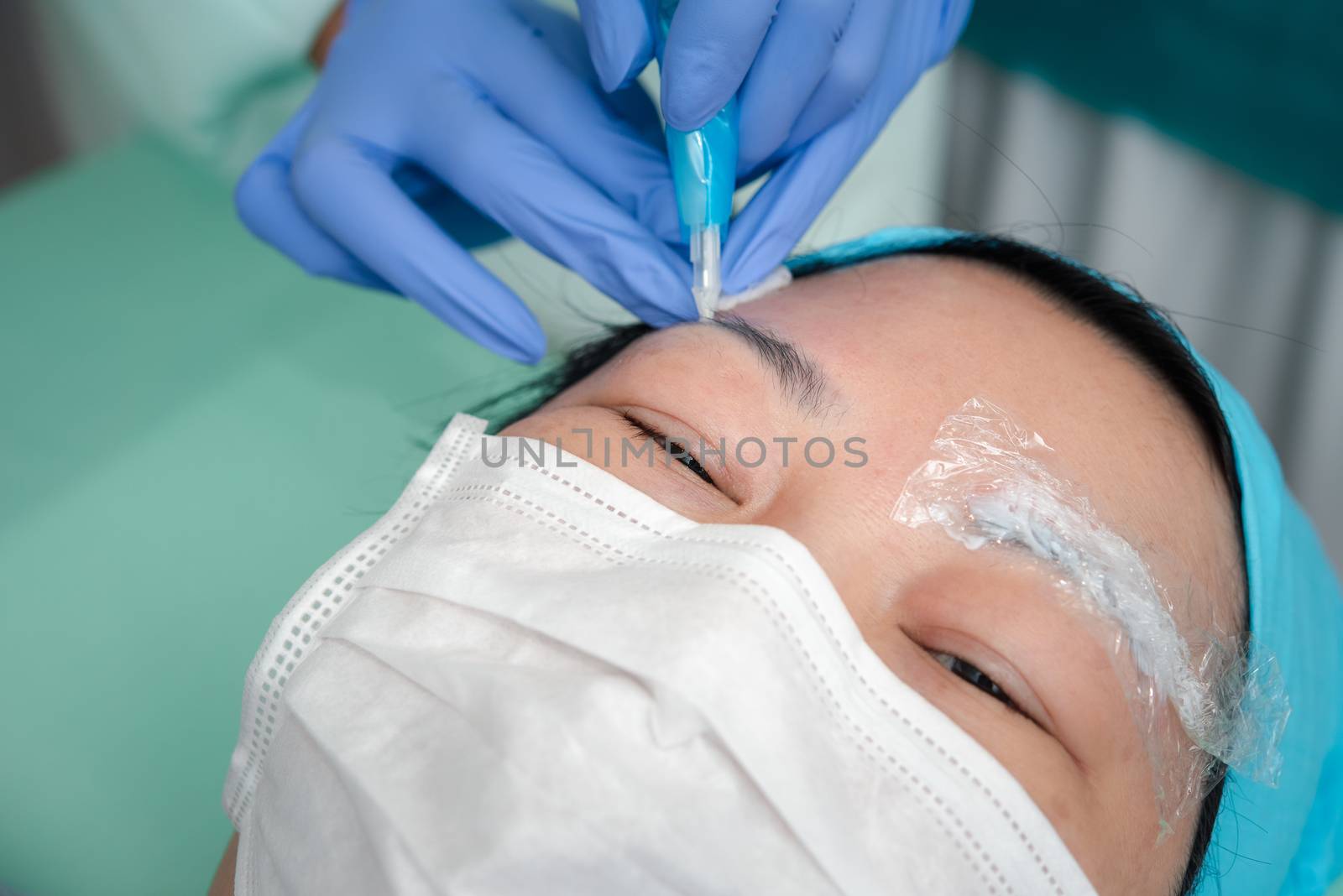 Asian woman eyebrow tattooing by doctor specialist in Eyebrow tattoo clinic or Eyebrow embroidery clinic for tattoo or correction use COVID-19 prevention policy protect by use mask and face shield