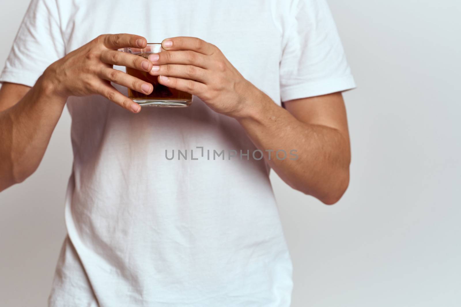 A man with a hot drink of tea in his hands in a white T-shirt on a light background cropped view by SHOTPRIME