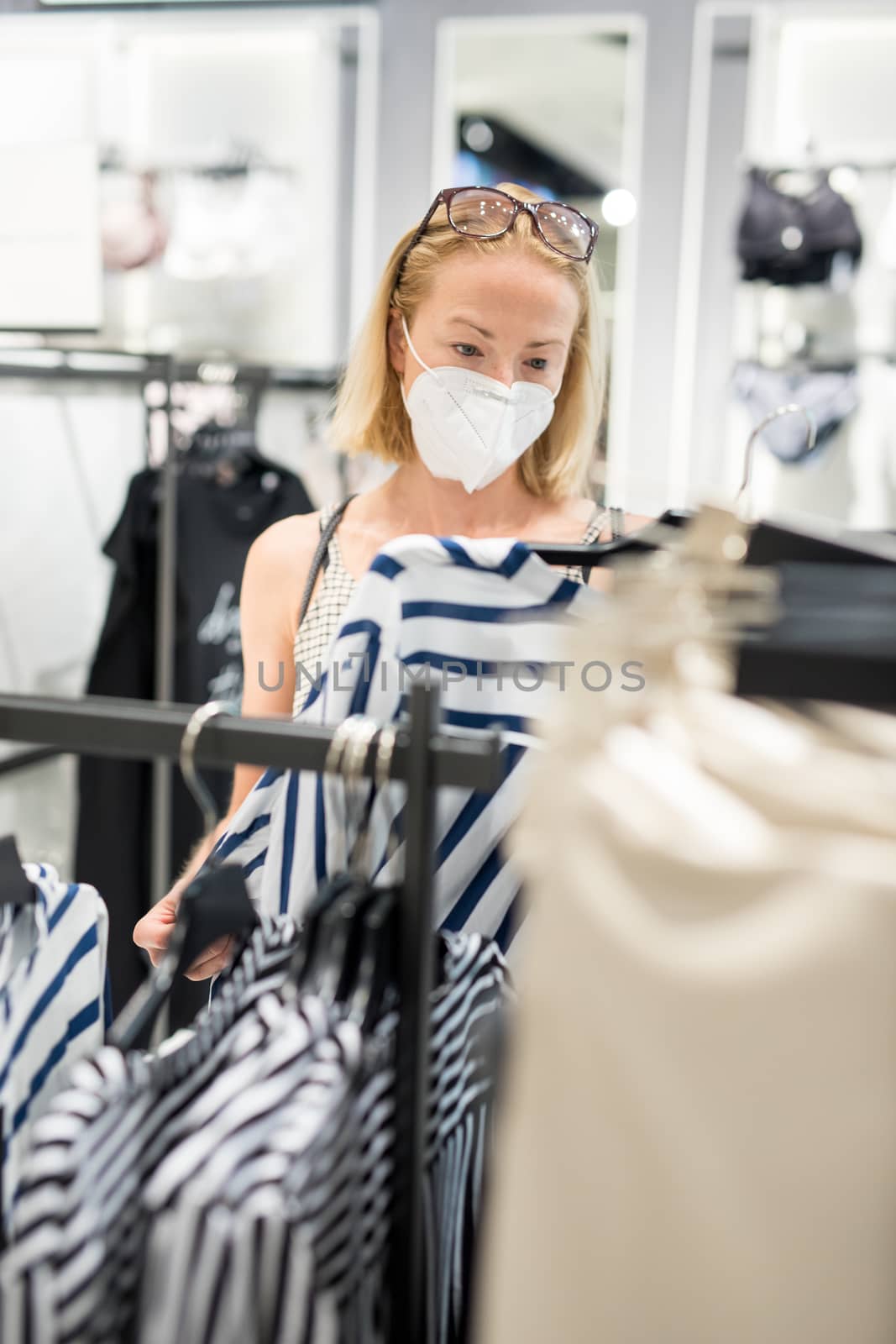 Fashionable woman wearing protective face mask shopping clothes in reopen retail shopping store. New normal lifestyle during corona virus pandemic.