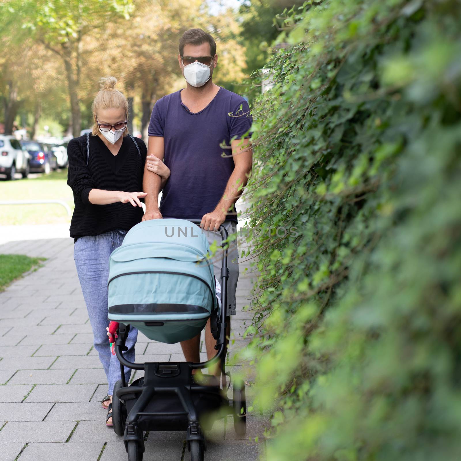 Worried young parent walking on empty street with stroller wearing medical masks to protect them from corona virus. Social distancing life during corona virus pandemic.