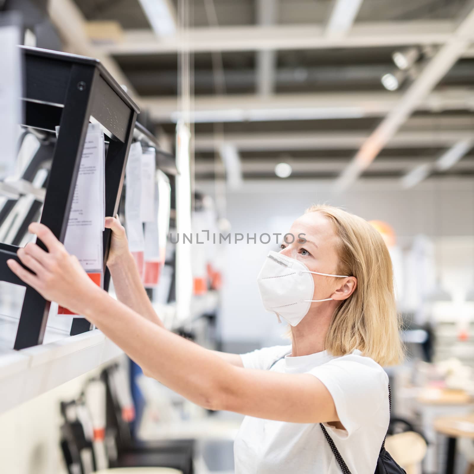 New normal during covid epidemic. Caucasian woman shopping at retail furniture and home accessories store wearing protective medical face mask to prevent spreading of corona virus.