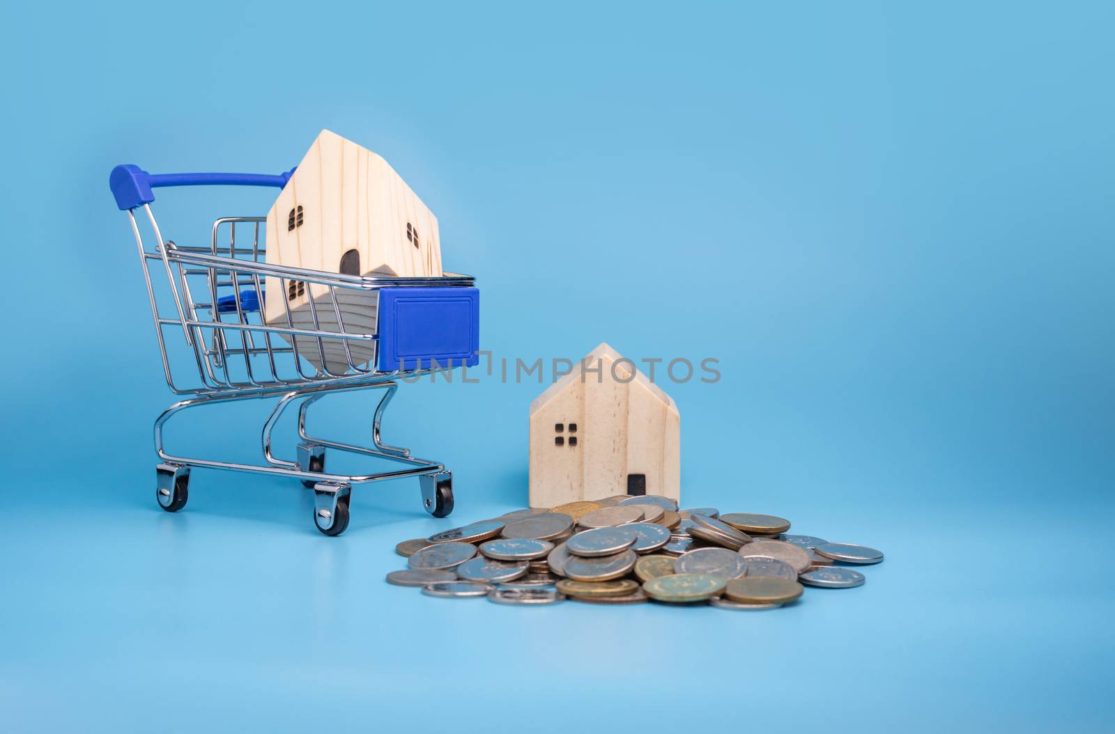 A model wooden house on a shopping cart With a pile of coins On a blue background. Mortgage concept. Money and house.