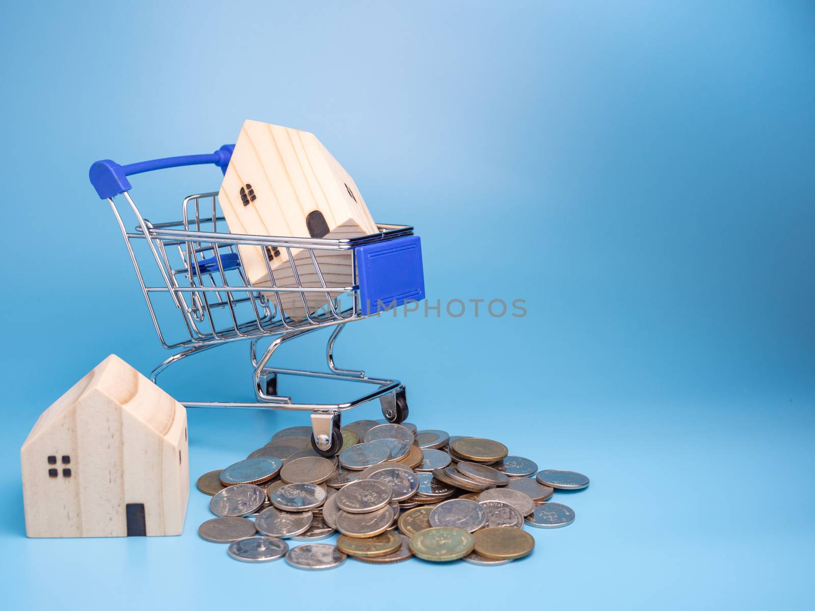A model wooden house on a shopping cart With a pile of coins On a blue background. Mortgage concept. Money and house.