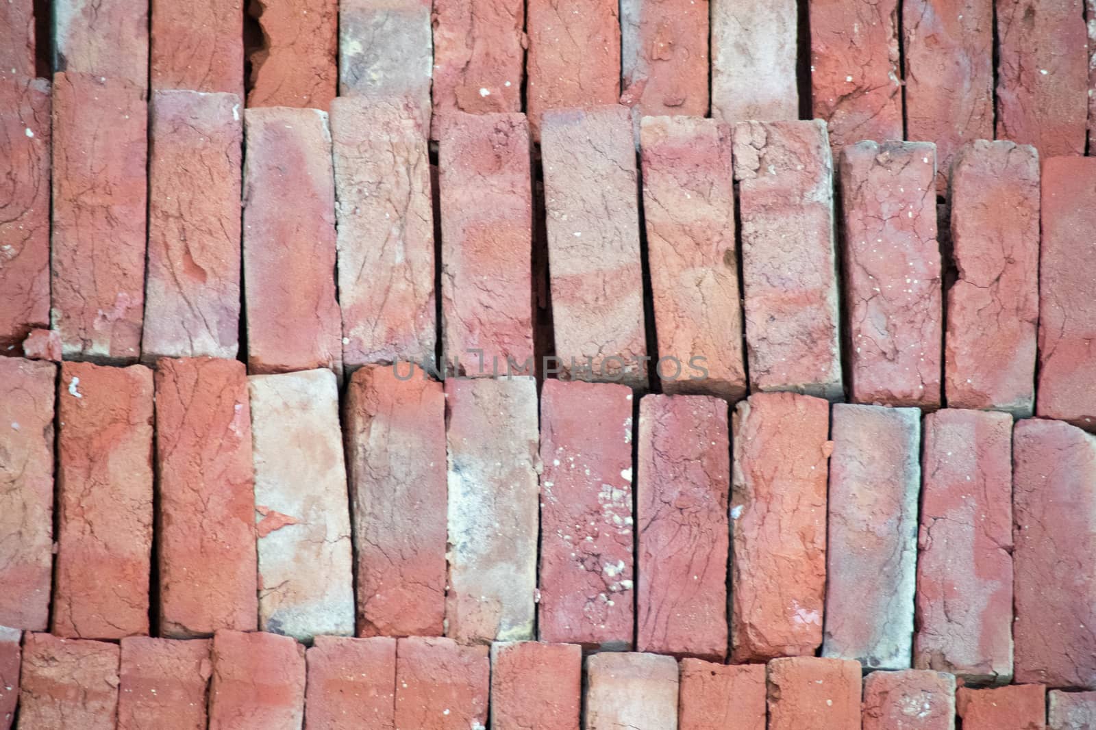 Pile of bricks placed on the ground, showing the pattern and the distinctive red color . Shows the clay klin fired bricks that are used for construction projects across india and are a major industry