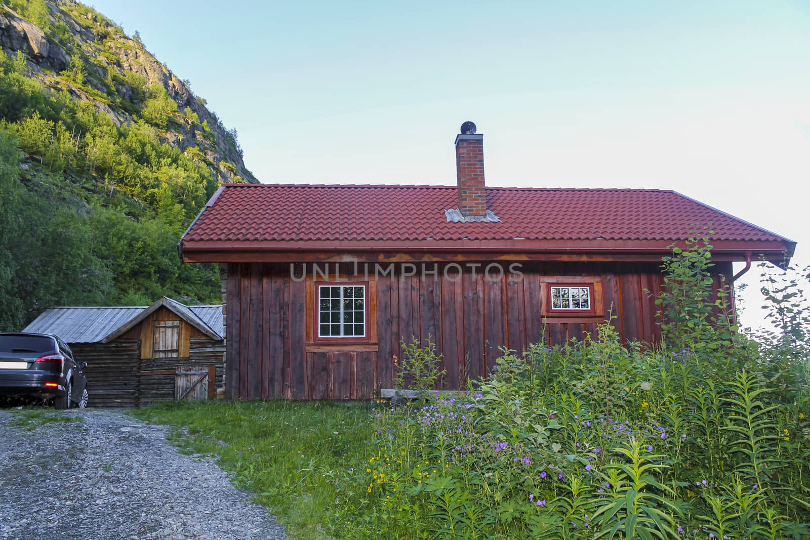 Old brown wooden cabin hut with a parked dark blue car in Hemsedal, Norway.