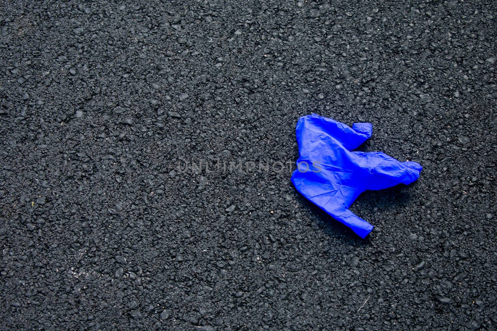 A Used Blue Medical Glove On a Blacktop Road To Protect From Coronavirus