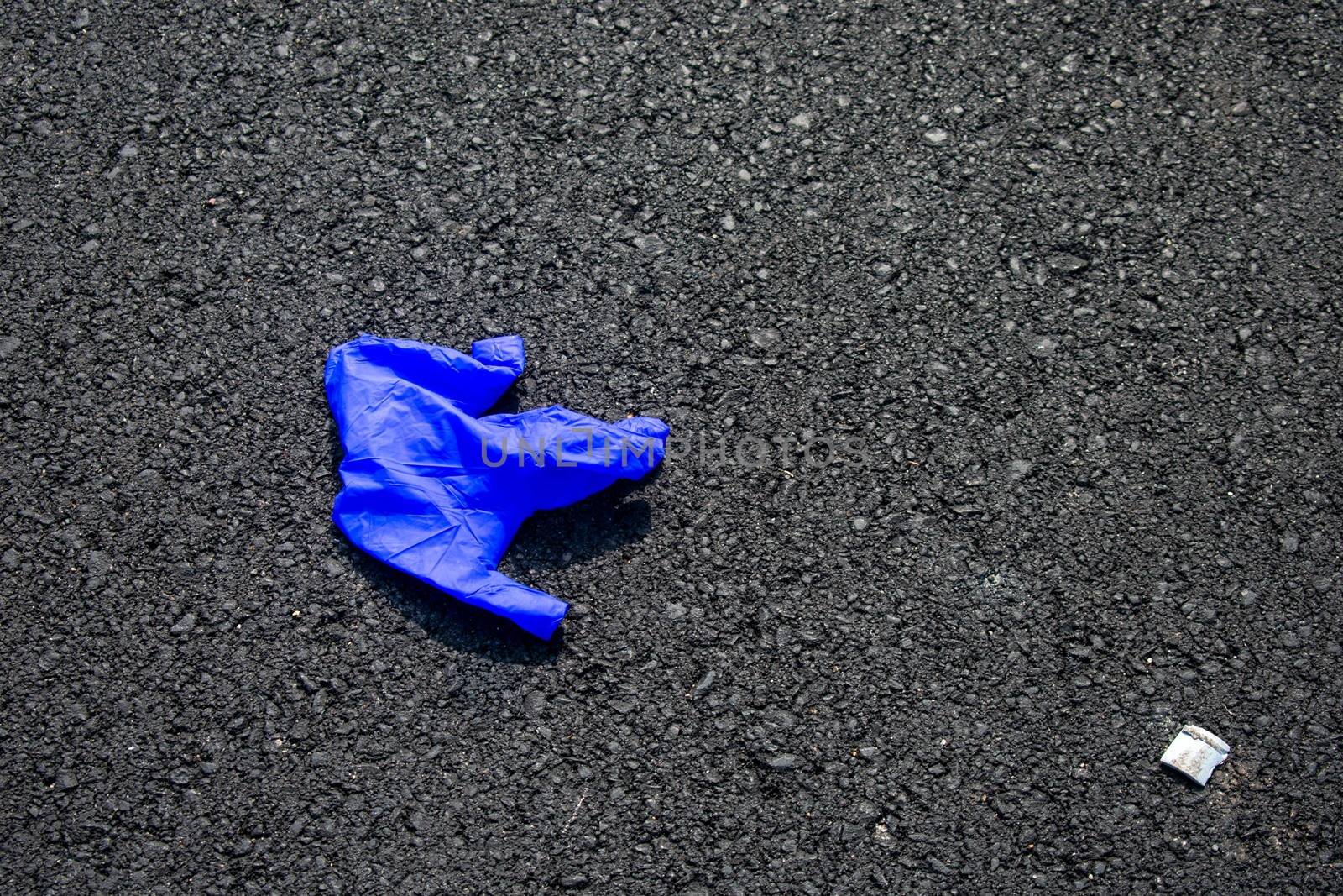 A Used Blue Medical Glove On a Blacktop Road To Protect From COV by bju12290